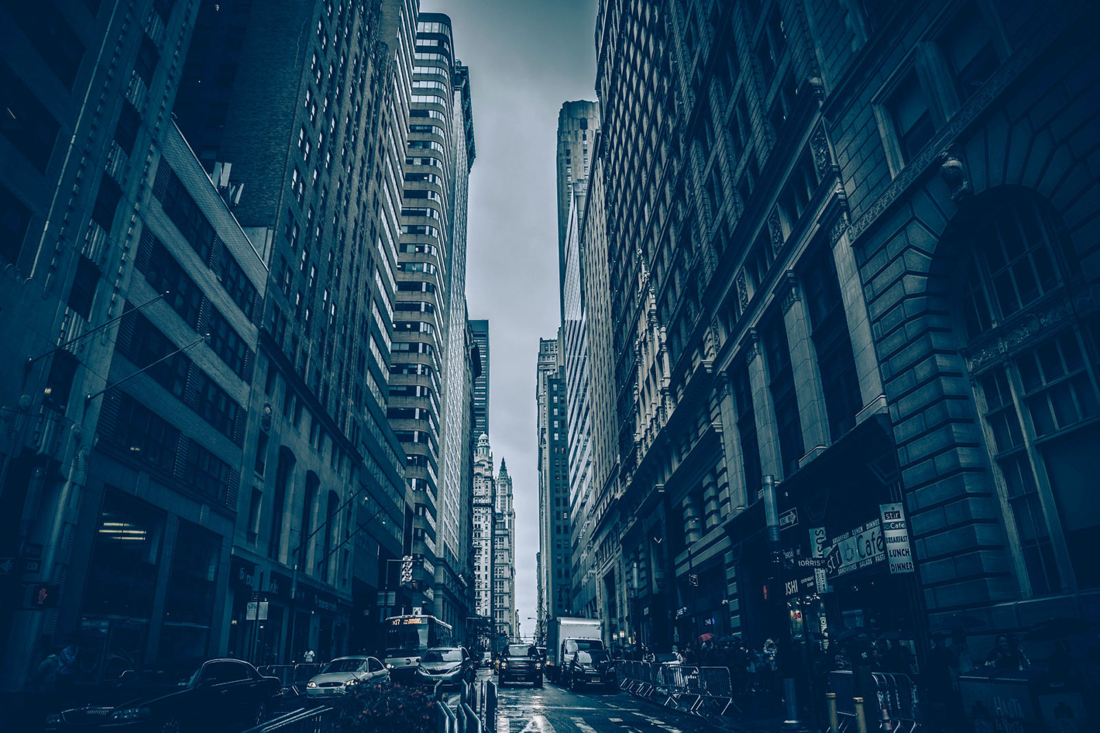 A moody urban street scene between tall buildings with cars.