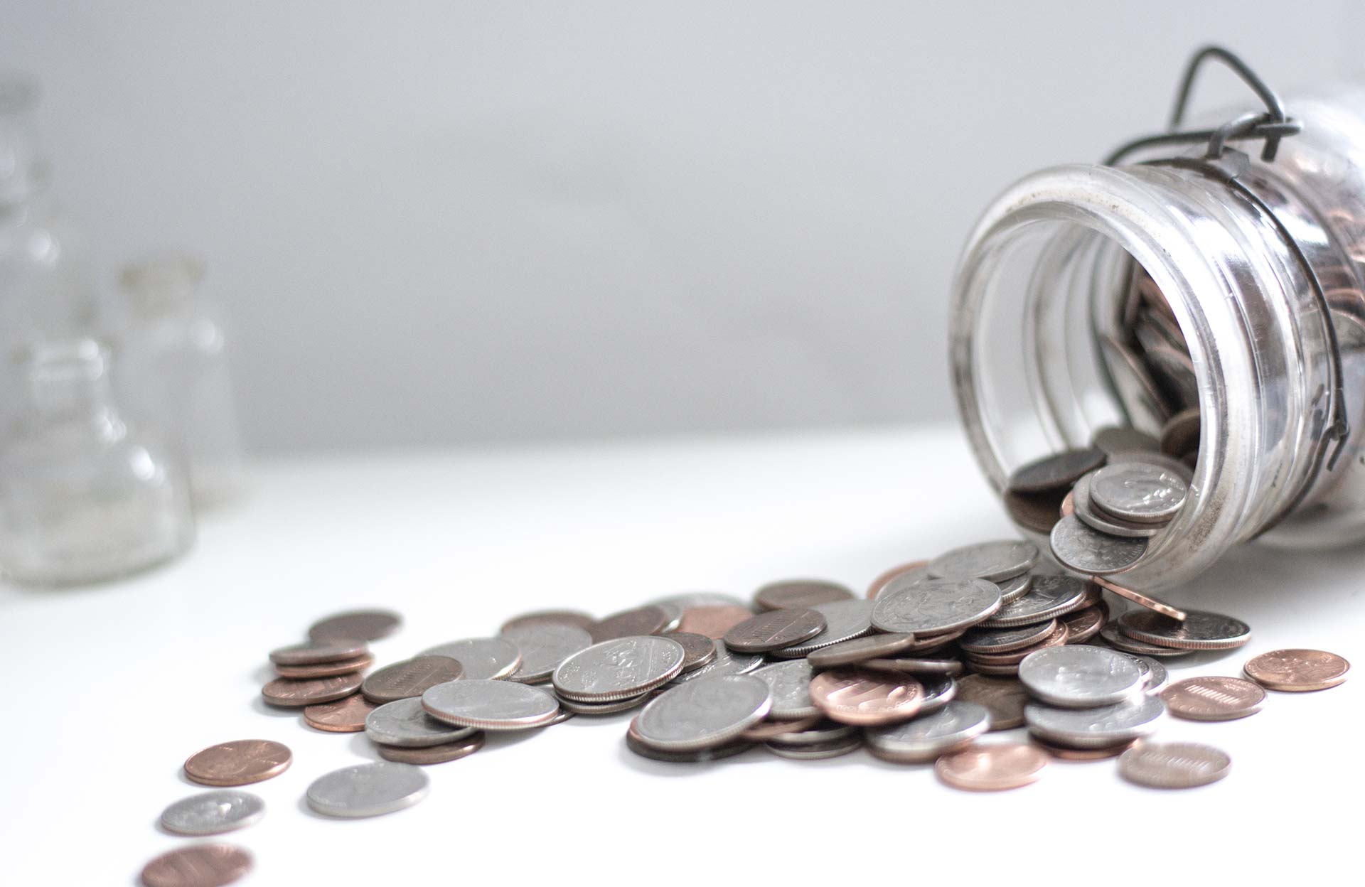 Coins spilling out of a jar on a white surface.