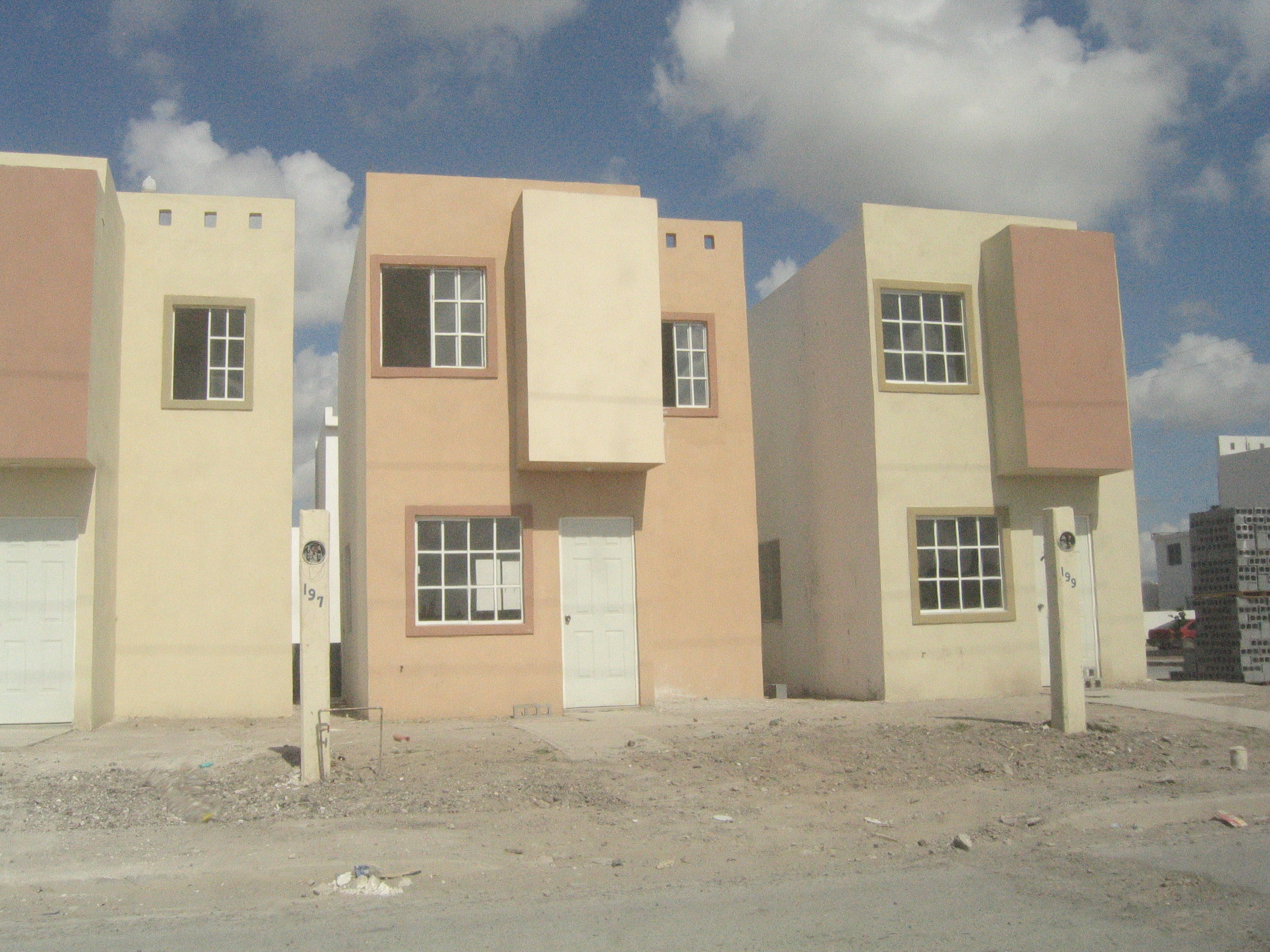 Row of simple, beige-colored houses under a partly cloudy sky.